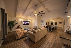 A spacious living room with a large sofa, a television, and a ceiling fan. - Beachfront Getaway: Fire Pit, Game Room & Views (Surfside)