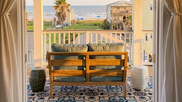Un balcon avec vue sur la plage, un banc en bois et un sol à motifs.