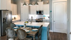 Une cuisine moderne avec des meubles blancs, un îlot central et un coin repas comprenant des chaises et une table.