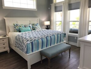 Une chambre à coucher avec un lit, une table de chevet, un banc et une fenêtre avec des rideaux.