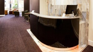 A reception desk with a dark counter, a wall-mounted TV, and a carpeted floor. - Best Western the Connaught Hotel (Wolverhampton)