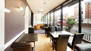 A modern interior with tables and chairs, large windows, and a view of the street. - Best Western the Connaught Hotel (Wolverhampton)