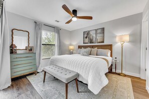 A bedroom with a bed, a bench, a dresser, a ceiling fan, a floor lamp, and a window with curtains. - Elegant Lakeview Escape - Top-rated, 2BR Condo steps from Marina, Dining, Fun (Kimberling City)