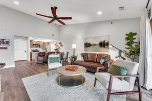 Ein geräumiges Wohnzimmer mit Deckenventilator, einem runden Couchtisch, einem braunen Ledersofa und einem Essbereich im Hintergrund.