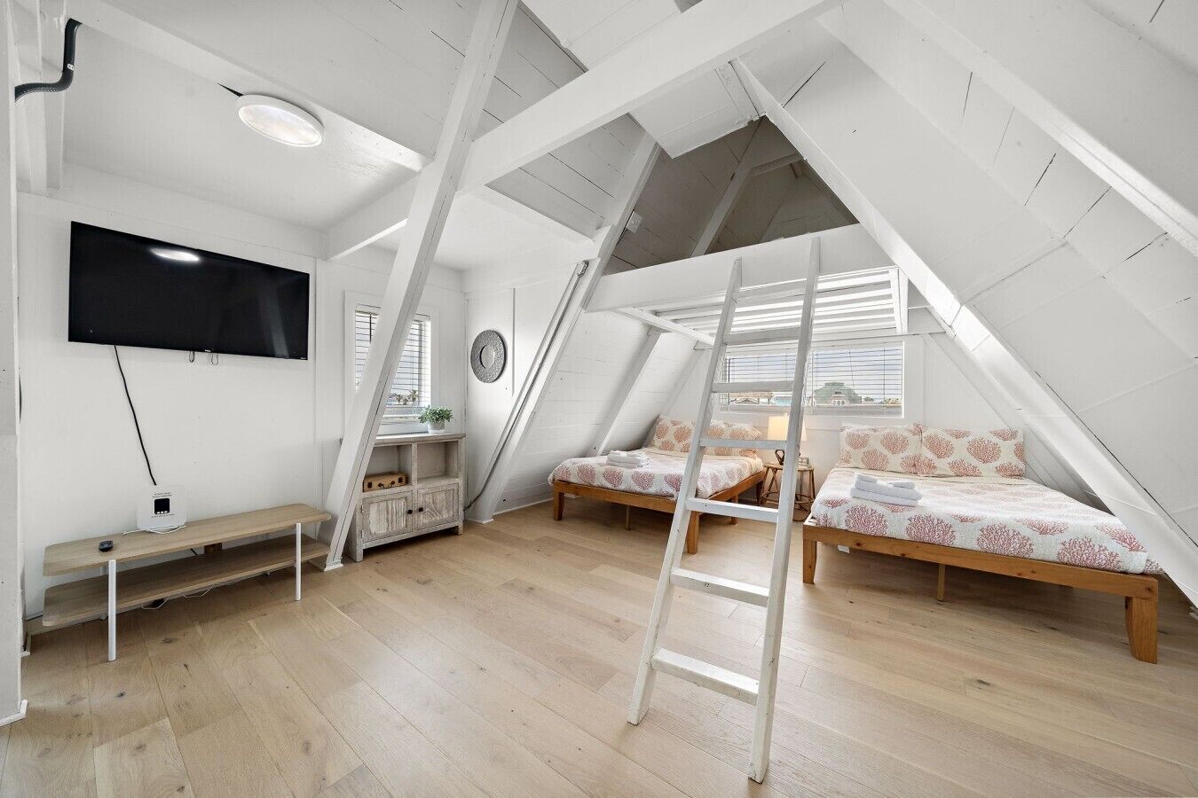 A loft bedroom with a TV, two beds, a ladder, and a wooden floor.