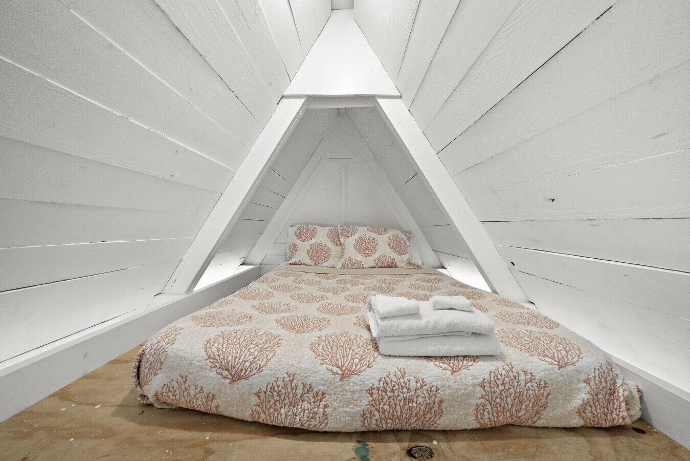 A triangular attic bedroom with a bed, pillows, and a neatly folded towel.