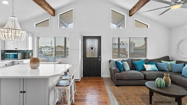 A spacious kitchen with a central island, a dining area with white chairs, a gray sofa with blue cushions, and a ceiling fan. - Canal Home with Two Docks and Large Gameroom (Surfside)