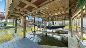 A wooden dock with a boat, a water feature, and a covered area with a view of the water. - Canal Home with Two Docks and Large Gameroom (Surfside)