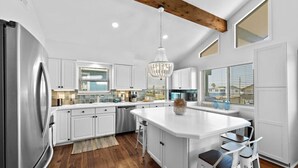 A modern kitchen with white cabinetry, a large island, stainless steel appliances, and a chandelier. - Canal Home with Two Docks and Large Gameroom (Surfside)