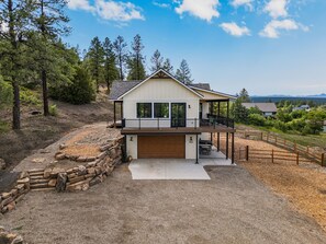 A two-story house with a covered porch, a garage, and a stone retaining wall. - Luxury Home on 5 Acres / Unreal Views! / Hot Tub! (Pagosa Springs)