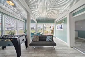A spacious indoor area with a foosball table, a sofa with cushions, and a view of a patio with outdoor seating.