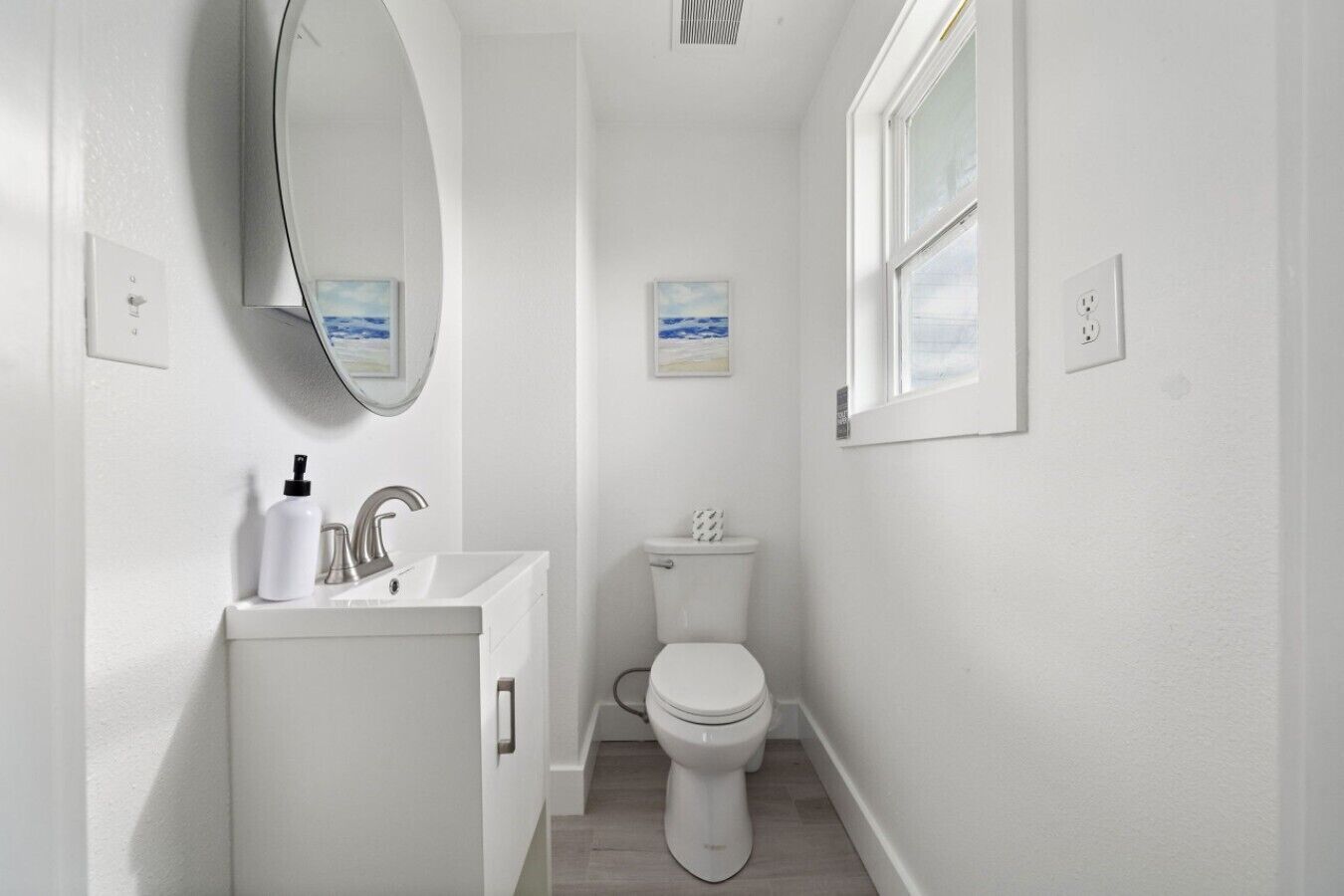 A compact bathroom with a sink, mirror, toilet, and a window.