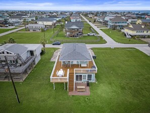 Une maison à deux étages dotée d’une terrasse, entourée d’une pelouse bien entretenue et offrant une vue dégagée sur l’océan.