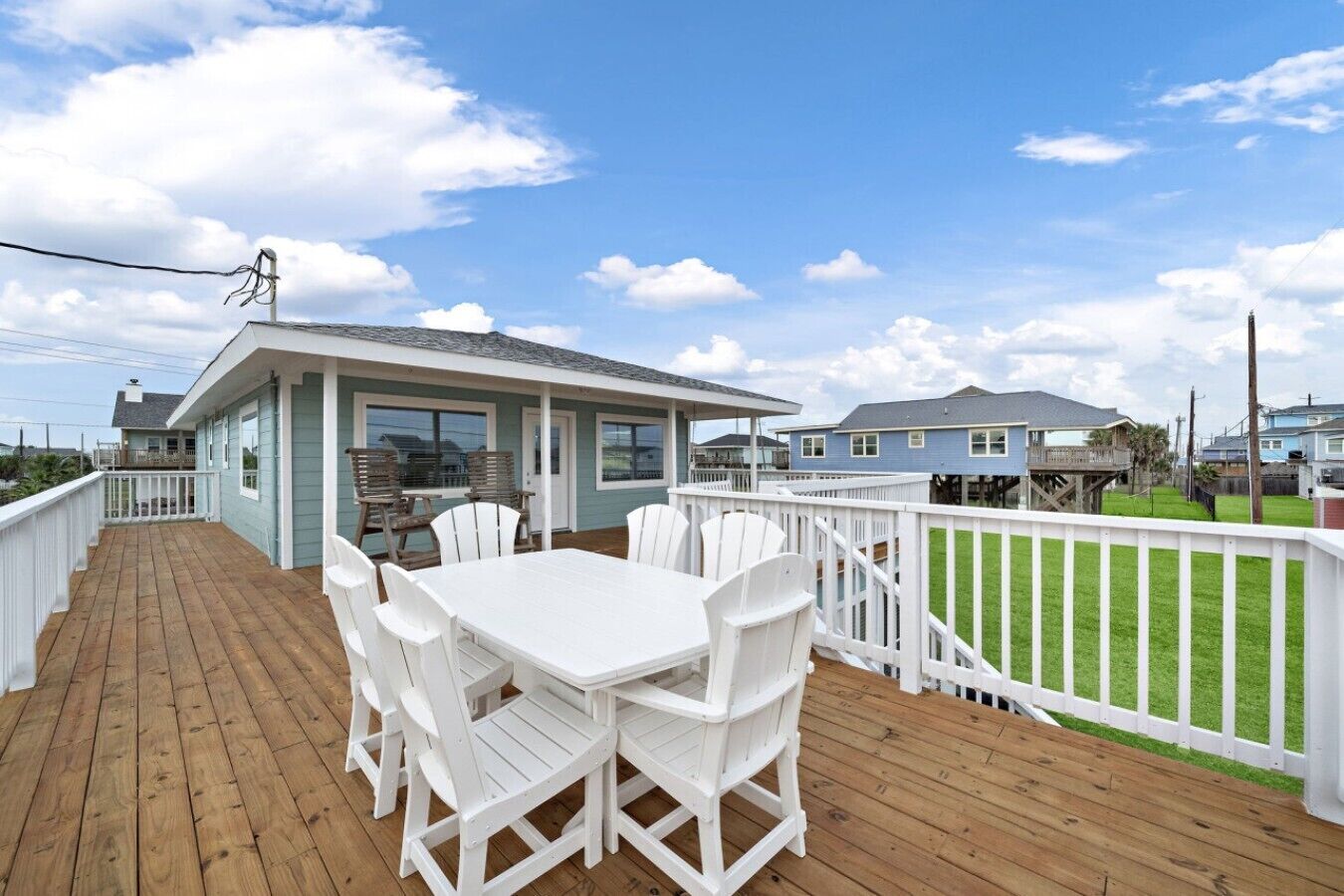 A wooden deck with a white table and chairs, a covered seating area, and a white fence.