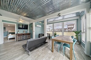 A spacious room with a wooden dining table, blue chairs, a grey sofa, and a TV on the wall.