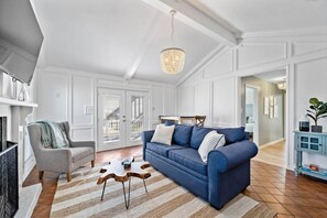 A living room with a blue sofa, a grey armchair, a wooden coffee table, and a chandelier. - Stunning Beach House, Ocean Views & Spacious Deck (Galveston)
