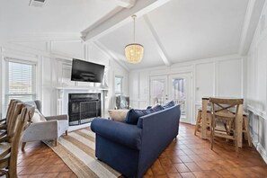 A living room with a fireplace, a television, a blue sofa, and a wooden dining table. - Stunning Beach House, Ocean Views & Spacious Deck (Galveston)