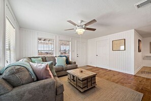 A living room with a sofa, a coffee table, a ceiling fan, and a door.