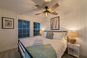 Ein Schlafzimmer mit einem Bett, einem Deckenventilator, einem Nachttisch und einem Fenster.