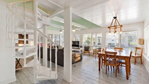 A spacious living area with a spiral staircase, a dining table with chairs, and a television in the background. - Texas Vacation Home with Pool, Near the Beach (Galveston)