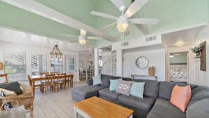 A spacious living room with a gray sofa, wooden coffee table, and ceiling fans. - Texas Vacation Home with Pool, Near the Beach (Galveston)