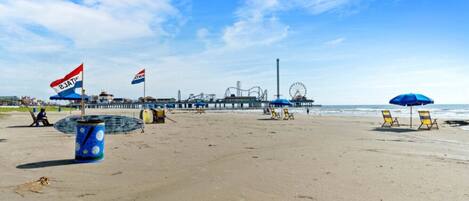 A beach with a pier, beach chairs, and flags.