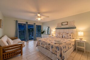 Une chambre à coucher avec un lit, une table de chevet, une chaise, un ventilateur de plafond et une vue par la fenêtre.