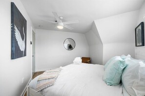A bedroom with a bed, a ceiling fan, a round mirror, and a framed picture on the wall. - Charming Home with Huge Deck, Steps from the Beach (Galveston)