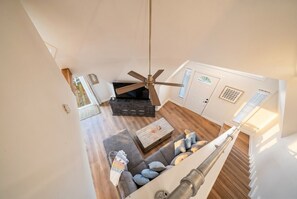 A modern interior with a ceiling fan, a sofa with cushions, a coffee table, and a staircase. - Charming Home with Huge Deck, Steps from the Beach (Galveston)