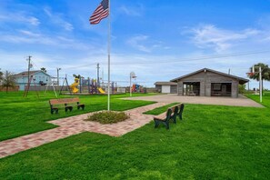 A playground with swings and slides, a picnic table, a bench, and a building with a garage. - Charming Home with Huge Deck, Steps from the Beach (Galveston)