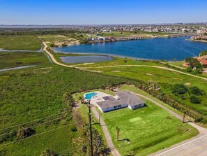 Uma casa com piscina, cercada por campos verdes e uma grande massa de água.