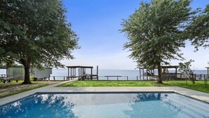 Une piscine avec vue sur la mer, entourée d’arbres et dotée d’une terrasse en bois.