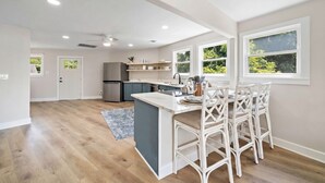 Une cuisine moderne avec un îlot central, des tabourets de bar blancs et une vue sur l’extérieur.