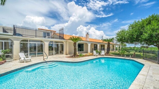 A swimming pool with a clear blue water, surrounded by a house with a balcony and a fence. - Villa with Private Pool, Game Room & 5+ Acres (Galveston)