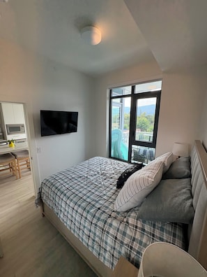 Ein Schlafzimmer mit Bett, Fernseher, Fenster und einer Küchenzeile.