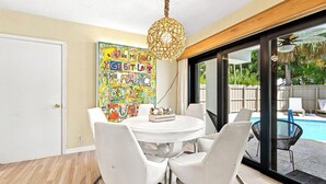 A dining area with a round table, white chairs, a colorful mural, and a view of a swimming pool. - Heated Pool, Sunny Oasis, 4 bedroom, 9 beds, 4 bathrooms (Fort Lauderdale)