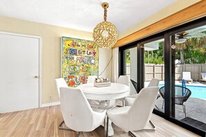 A dining area with a round table, white chairs, a colorful mural, and a view of a swimming pool. - Heated Pool, Sunny Oasis, 4 bedroom, 9 beds, 4 bathrooms (Fort Lauderdale)