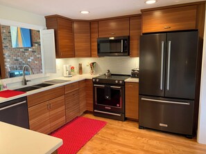 Eine moderne Küche mit Holzausstattung, Edelstahlgeräten, einer Mikrowelle, einem Kühlschrank und einem roten Teppich.