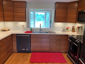 Een moderne keuken met houten kastjes, een vaatwasser, een rood kleed en een raam met uitzicht op groen.