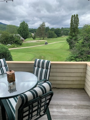 Een terras met een glazen tafel en gestreepte stoelen, met uitzicht op een golfbaan.