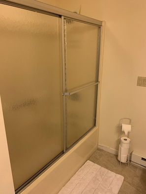Een badkamer met een douchecabine van glas, een toiletrolhouder en een witte vloerkleed.