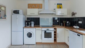 Een compacte keuken met een wasmachine, een magnetron, een koffiezetapparaat, een broodrooster en een boek getiteld 'Chocolat Menier' op het aanrecht.