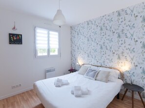 Ein Schlafzimmer mit einem Bett, einem Fenster, einer Heizung und einer Wand mit floralem Muster.