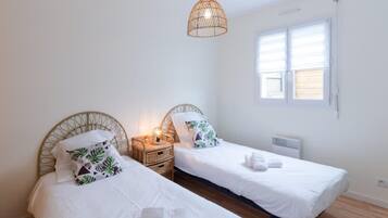 A bedroom with two single beds, a bedside table with a lamp, and a window with blinds.