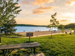 Ein Strand mit Picknickbereich, einer Holzbank, einem Schild und Blick auf den See.