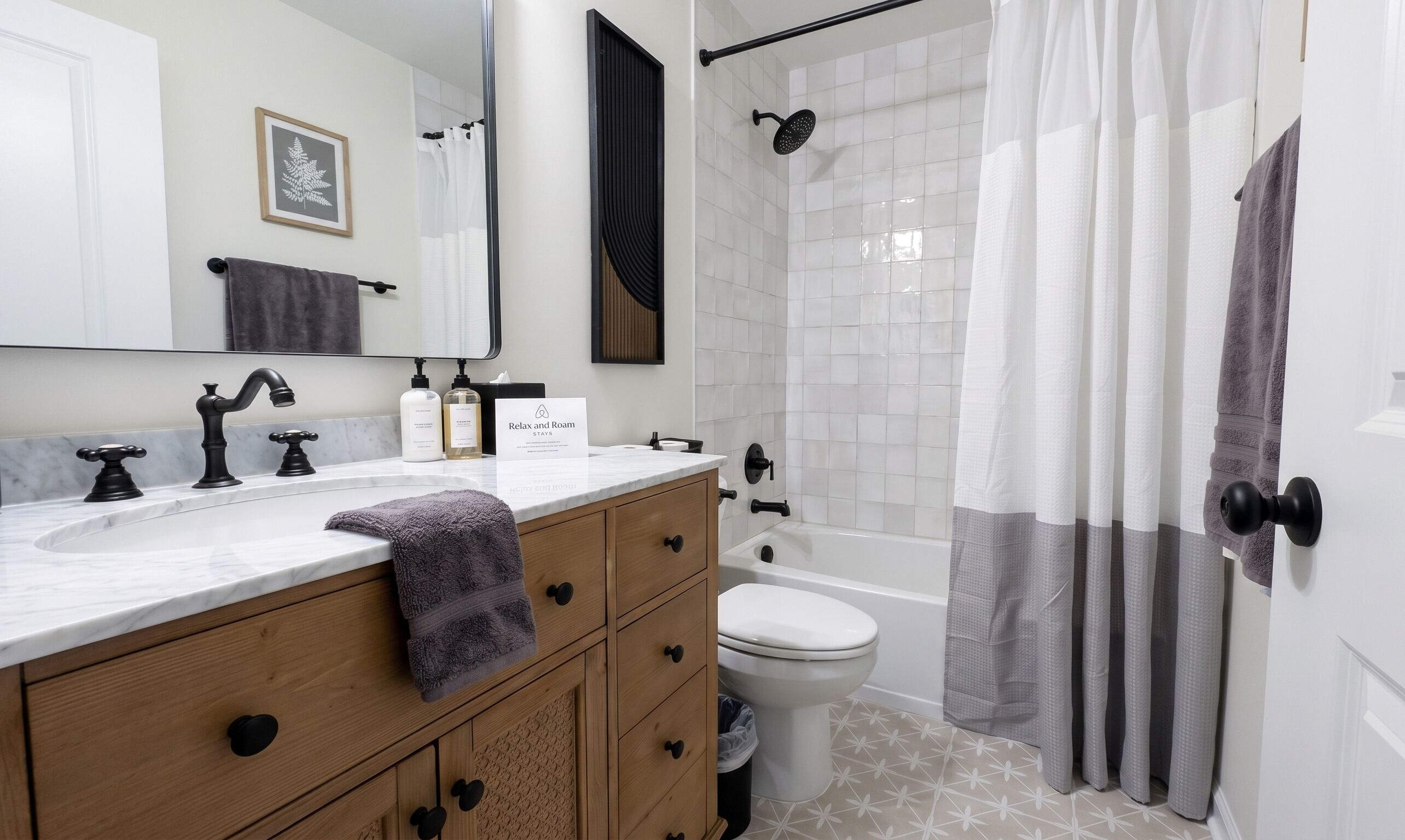 A bathroom with a white sink, black faucets, a wooden vanity, a toilet, a shower with a glass door, and a towel hanging on the wall.
