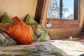 Ein Bett mit einem blumigen Überwurf, einem grünen Kissen und einem orangen Kissen.