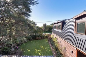 Ein modernes Gebäude mit einer geneigten Dachfläche, einem kleinen Garten mit Rasen und einer Holzterrasse.