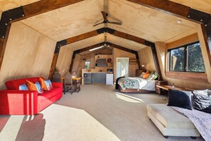 A spacious loft bedroom with a large bed, a red sofa, and a desk area. - Roberts Retreat - Auckland Holiday Home (Laingholm)