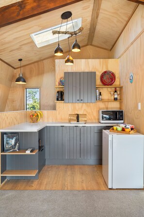 A compact kitchen with wooden cabinetry, a microwave, a refrigerator, and a fruit basket. - Roberts Retreat - Auckland Holiday Home (Laingholm)
